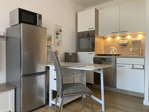 Une cuisine compacte équipée d’un réfrigérateur, d’un four à micro-ondes, d’un four traditionnel et d’un petit coin repas avec une chaise et une table.