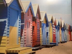 Eine Reihe bunter Strandhäuser mit geneigten Dächern und hölzernen Bänken davor.