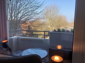 Un balcon avec une table et des chaises, une balustrade et une vue sur les arbres et les bâtiments.