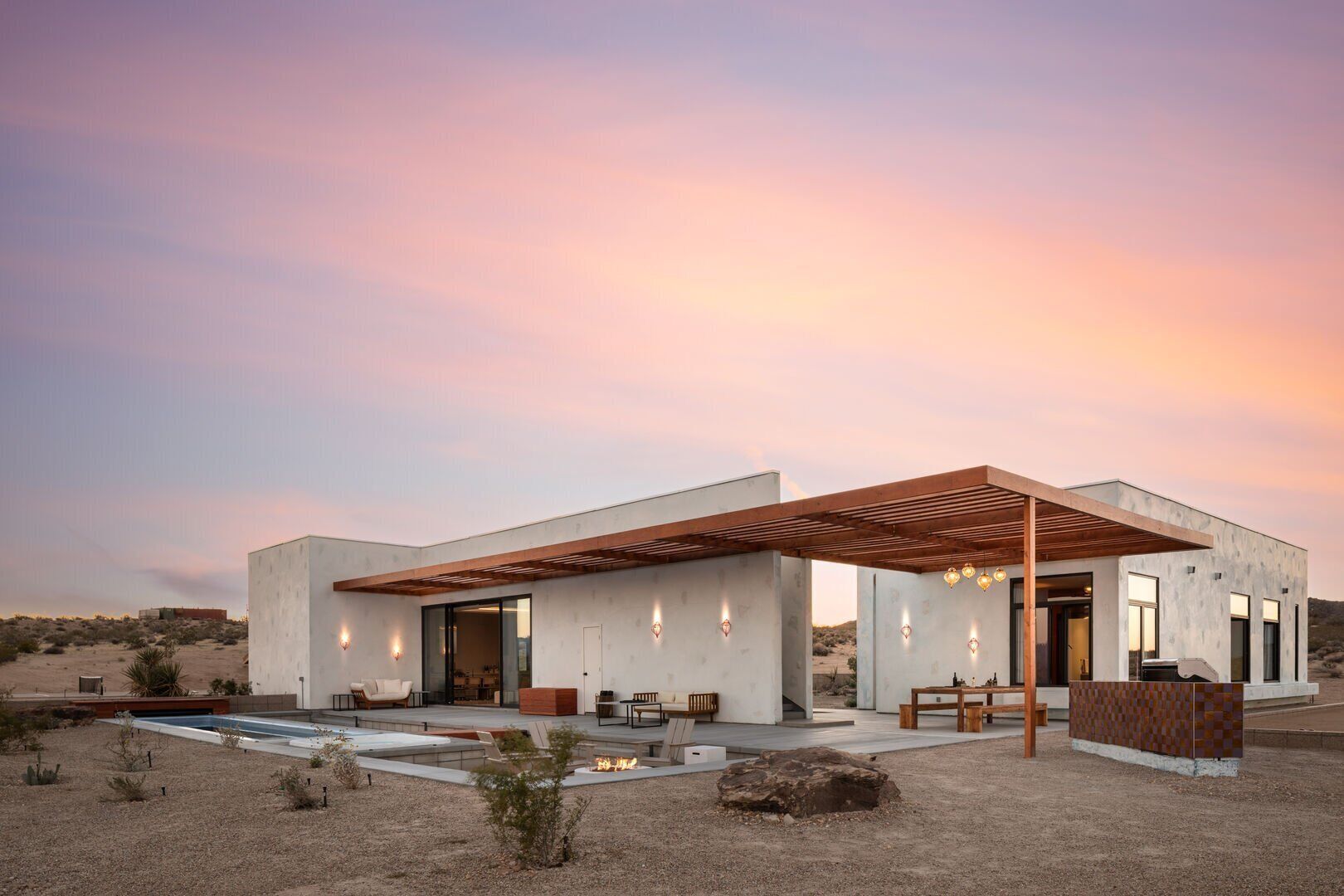 Une maison moderne dotée d’un patio couvert, d’une piscine et surplombant un paysage désertique.