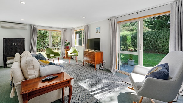 Un salon spacieux comprenant un canapé, un fauteuil, un téléviseur et une grande porte-fenêtre coulissante donnant sur un jardin.