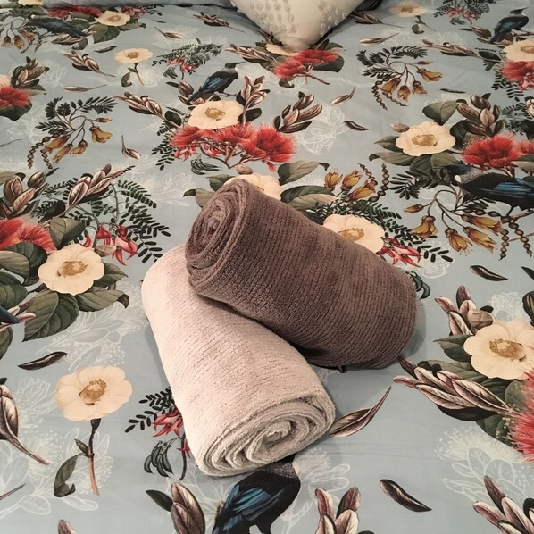Una cama con una colcha estampada con motivos florales y dos toallas enrolladas.