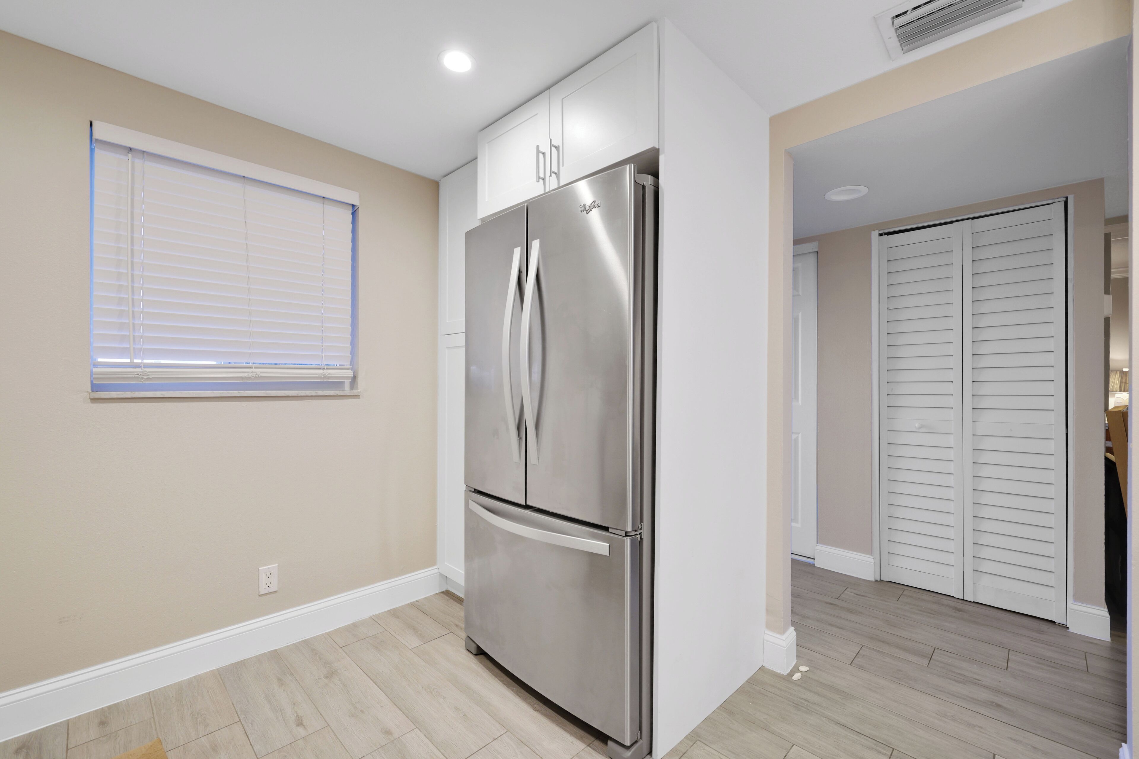 A modern kitchen with a stainless steel refrigerator, beige walls, and a window with blinds.