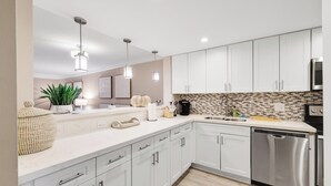 A modern kitchen with white cabinets, a stainless steel dishwasher, and pendant lighting. - Stylish 2BR, 2BA Apartment with Balcony & Pool - Just Steps from the Beach (Boca Raton)