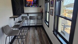 A bar area with bar stools, a television screen, and a window with a view of the outdoors.
