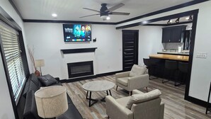 A modern living room with a fireplace, sofa, armchairs, and a TV mounted on the wall.