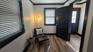 A hallway with wooden flooring, a bench, a wall-mounted light, and a door leading to another room.