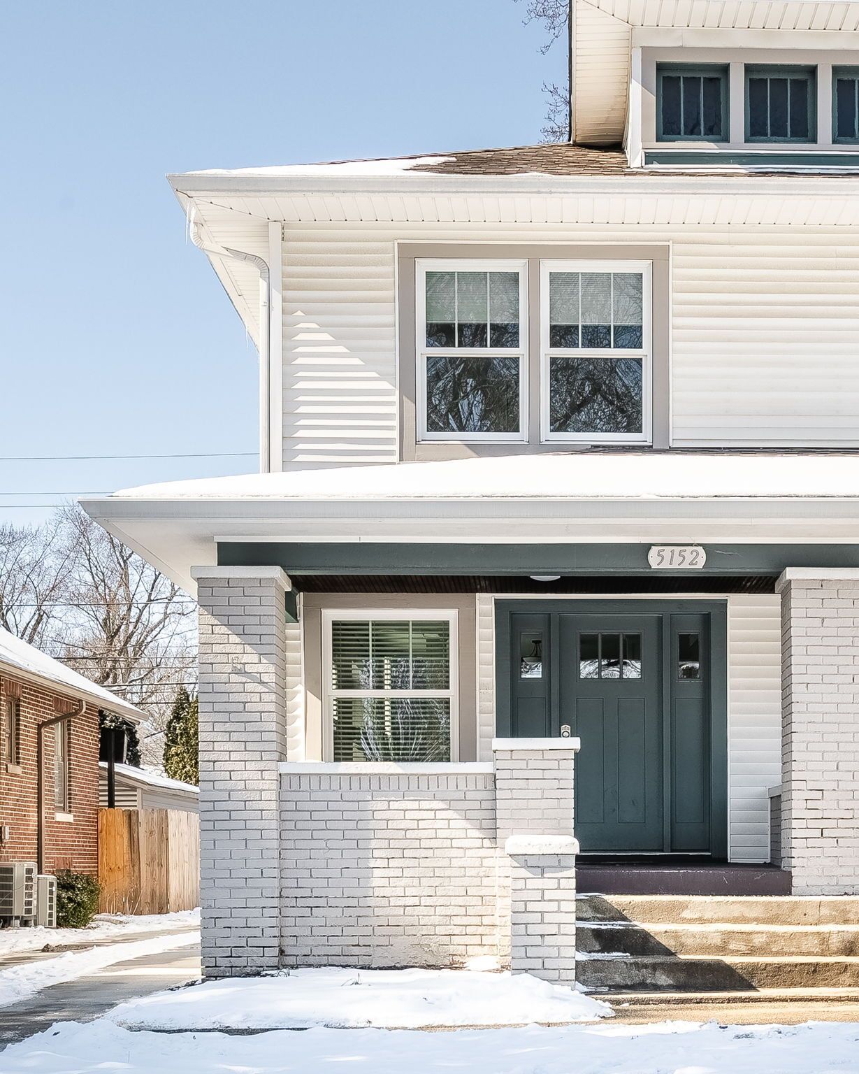 A two-story house with a dark front door, white siding, and a brick entryway.