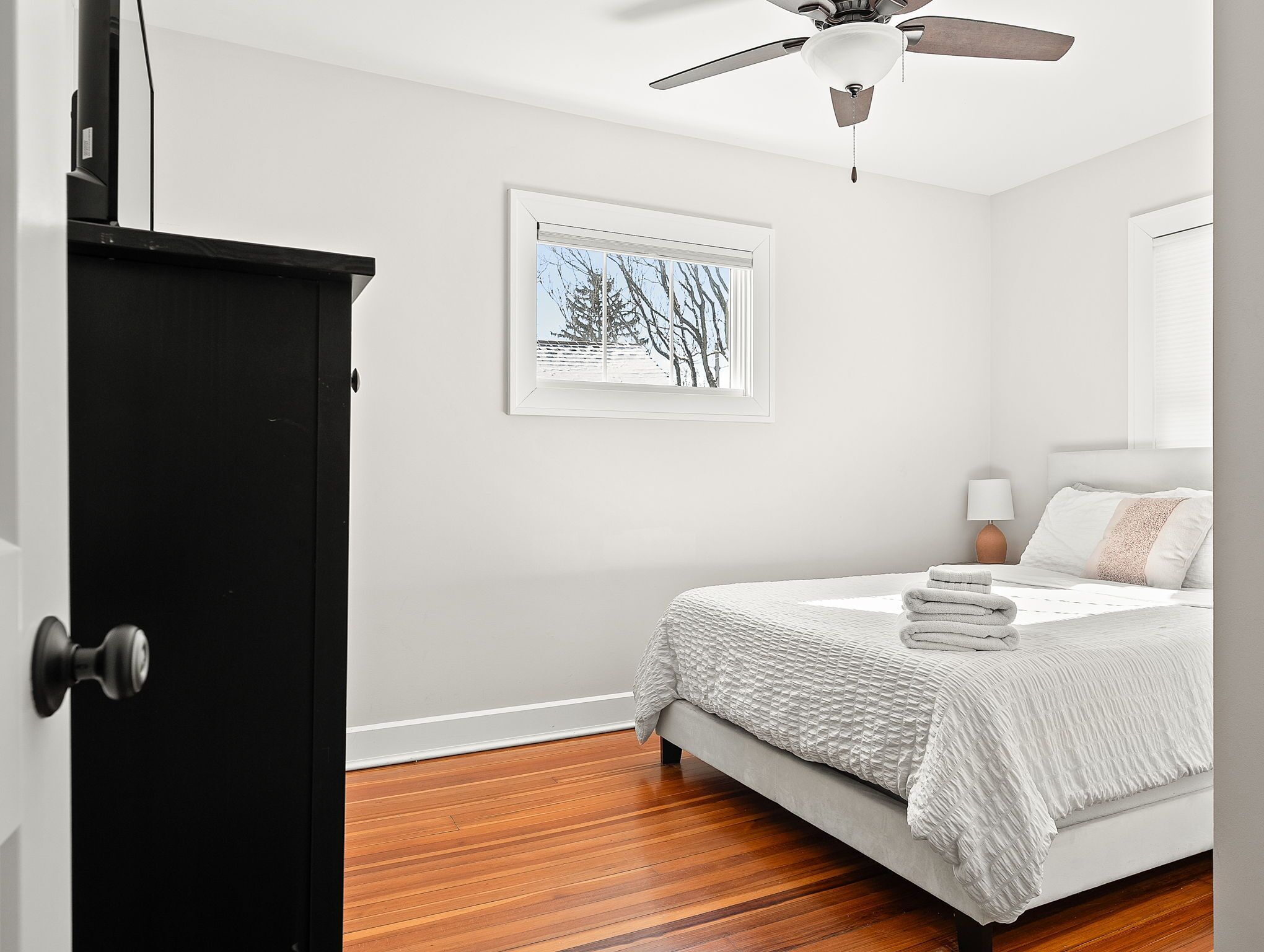 Une chambre à coucher avec un lit, un ventilateur de plafond, un tableau encadré et un plancher en bois.