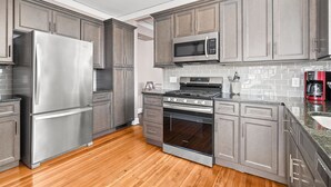A modern kitchen with stainless steel appliances, grey cabinetry, and a tiled backsplash. - Adorable Broad Ripple Duplex (Indianapolis)