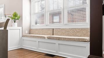A room with a built-in bench with patterned cushions, a potted plant, and a window with blinds.