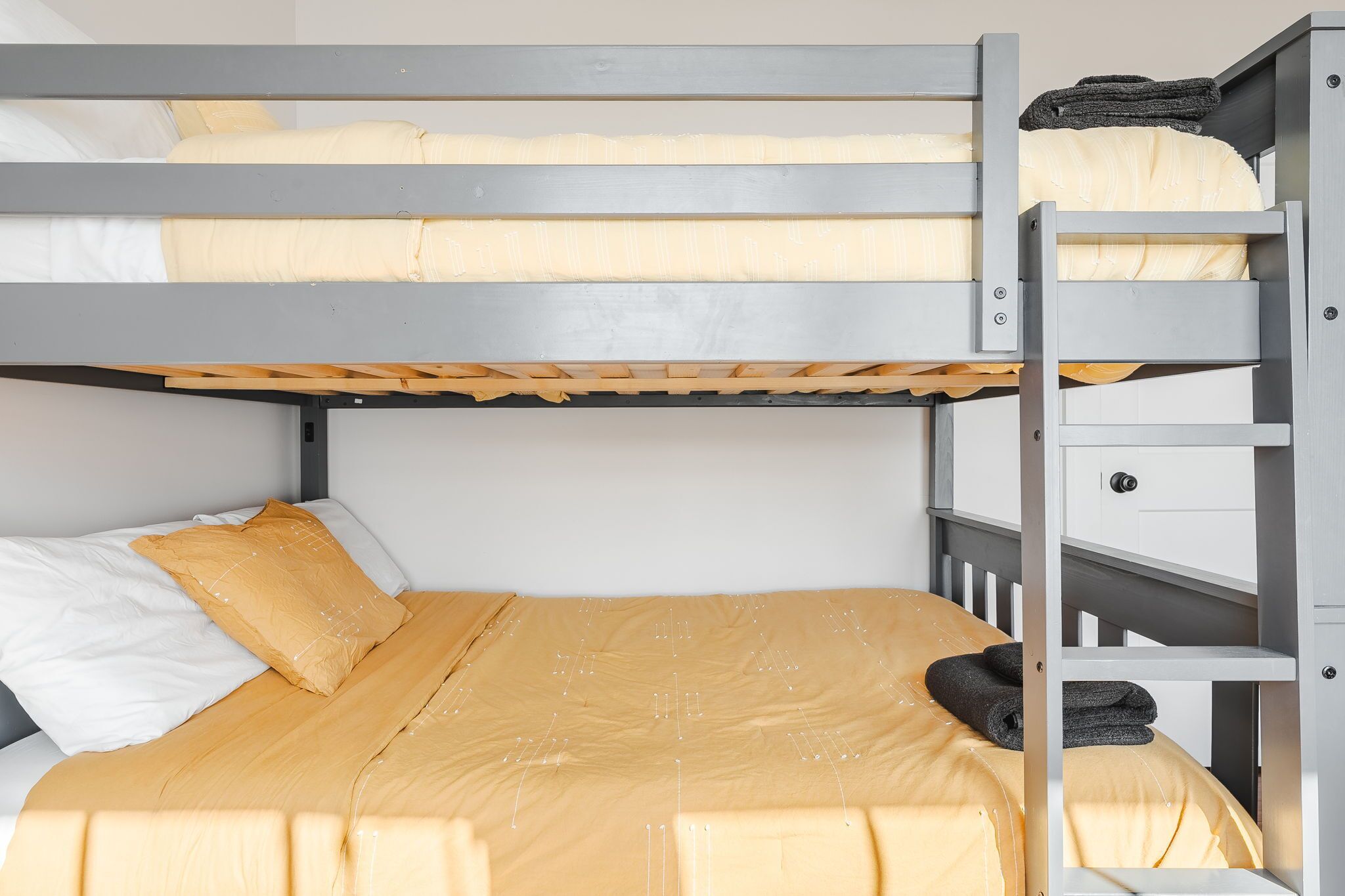 Ein Stockbett mit einer Leiter, ein Bett mit einer gelben Tagesdecke und ein weißes Kopfkissen.