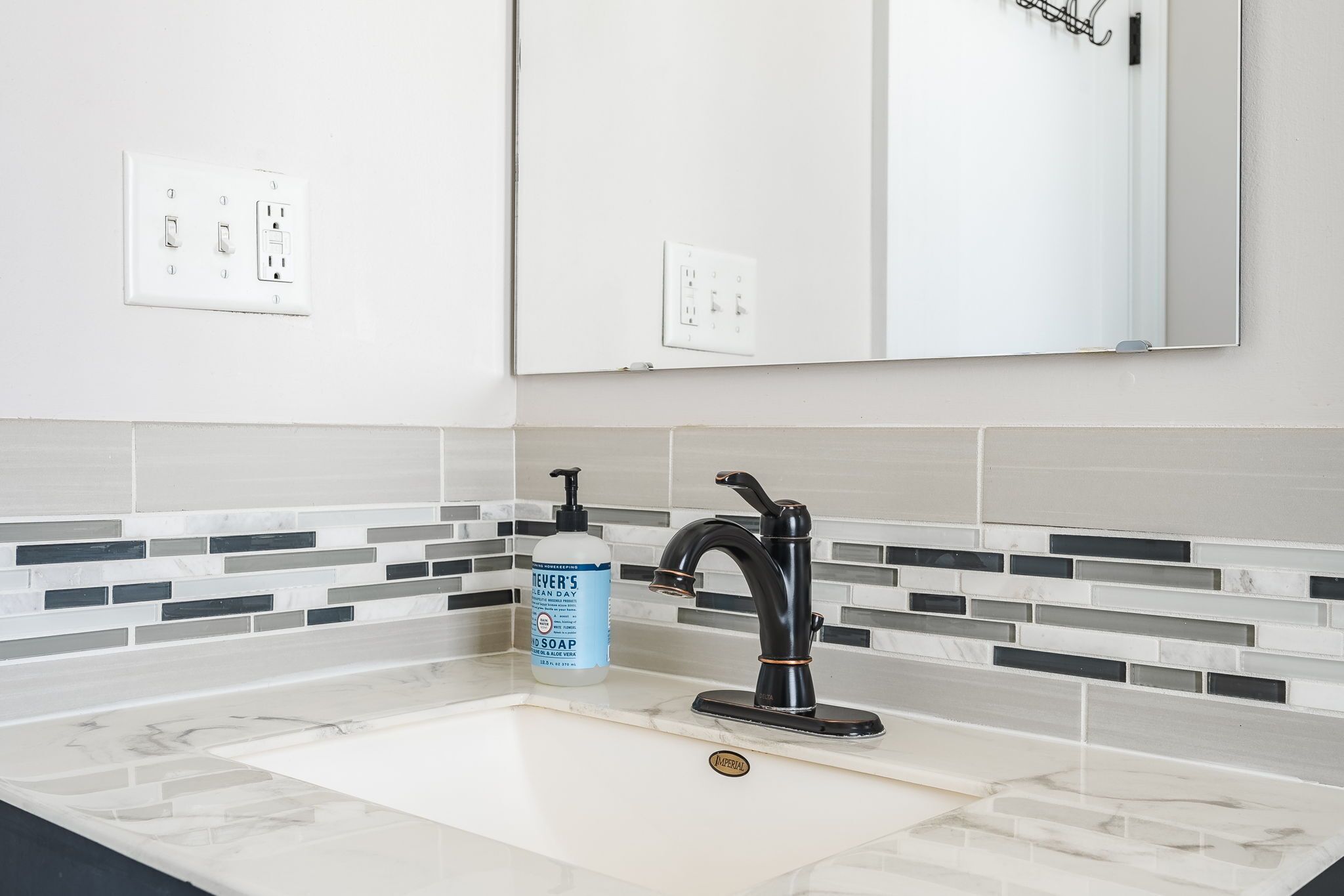 Une salle de bain avec un lavabo blanc, un robinet noir et un flacon de savon.