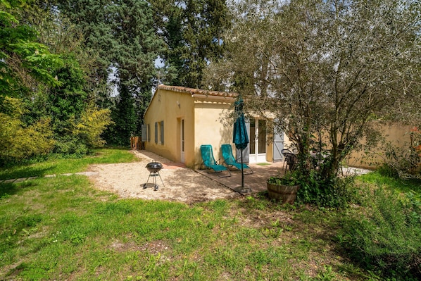 A small house with a patio, a barbecue grill, and two green chairs. - Holiday Home 'Maisonnette' with Private Terrace, Garden and Wi-Fi (Le Thor)