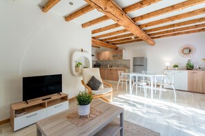 A modern living room with a TV, wooden furniture, a dining area, and a kitchen in the background.