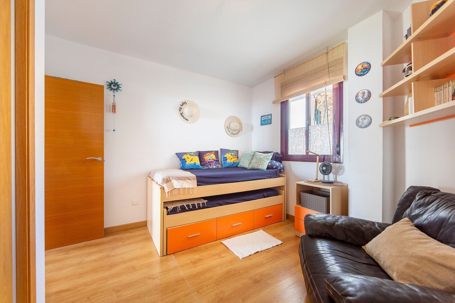 A bedroom with a bed, a dresser, a window, a fan, and a couch.