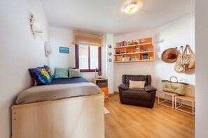 A bedroom with a bed, a chair, a shelf with books, and a wall with a sign.