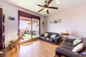 A living room with a sofa, a coffee table, a ceiling fan, and a view of the outside.