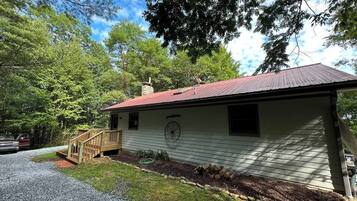 A single-story house with a red roof, a wooden deck, and a gravel driveway.