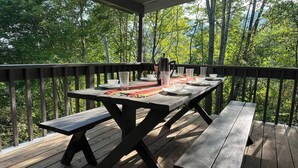 Eine Holzterrasse mit Picknicktischen und -stühlen, umgeben von Bäumen.