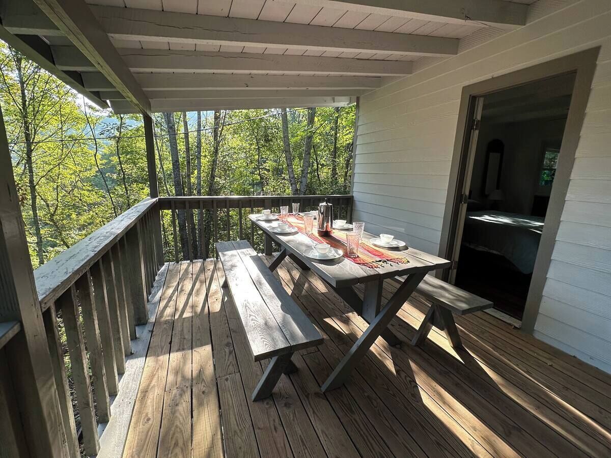 A wooden deck with a picnic table set up, overlooking a forested area.