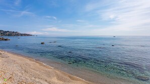 A clear beach with calm waters, a sandy shore, and a distant shoreline with buildings.