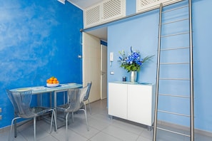 A modern kitchen with a blue wall, a white cabinet, a metal ladder, and a dining area with chairs and a table. - Casa Mare Sea View with Air Conditioning (Giardini Naxos)