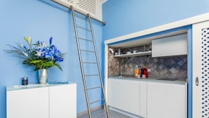 A kitchen with white cabinets, a blue wall, a ladder, a vase with flowers, and a coffee machine.