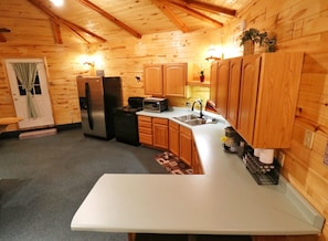 Interno di una baita in legno con una cucina dotata di frigorifero, fornello, microonde e pensili in legno.