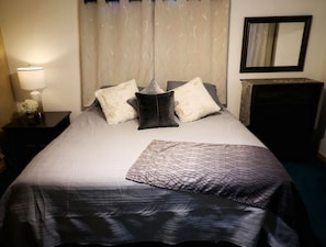 Un letto rifatto con una coperta fantasia, una lampada da comodino e uno specchio appeso al muro.