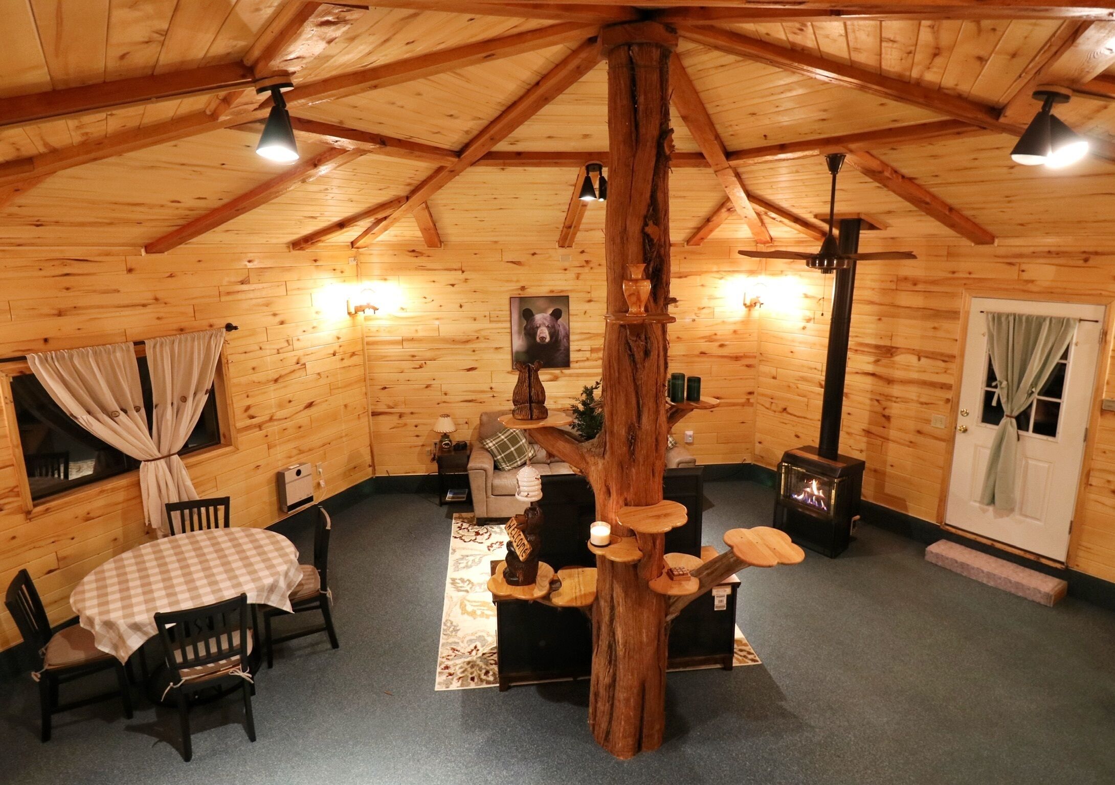A cozy log cabin interior with a dining table, chairs, a fireplace, and a tree sculpture.