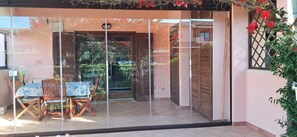 A glass door leading to a patio with a table and chairs, a wooden door, and a view of a garden. - Apartment 'Casa Papaya' with Shared Pool, Wi-Fi and Air Conditioning (murta maria)