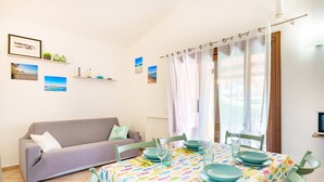 Et spiseområde med et bord dækket til fire personer, en sofa og et vindue med gardiner.