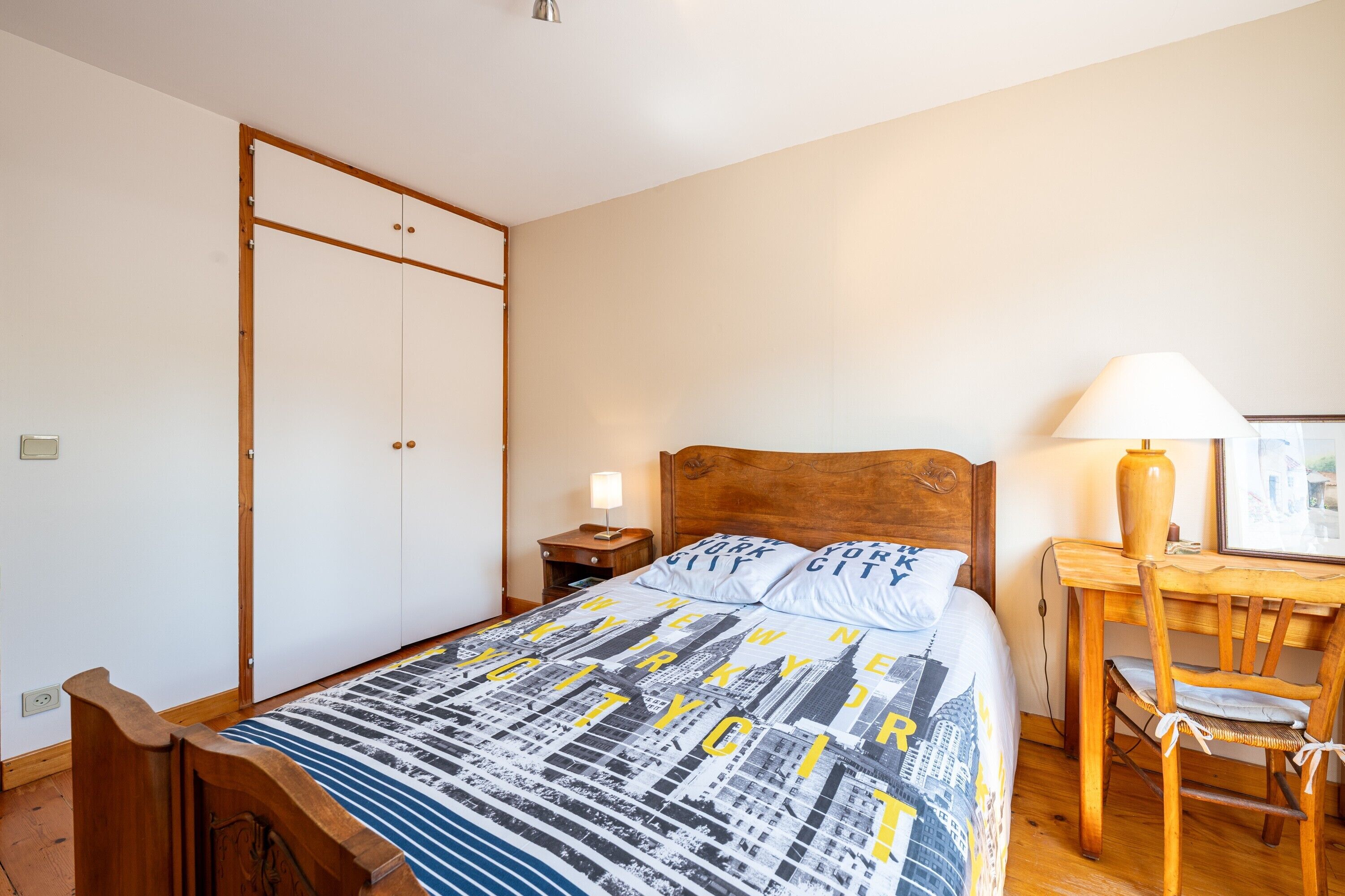 Un dormitorio con cama, un escritorio de madera, una silla, una mesita de noche y un guardarropa.