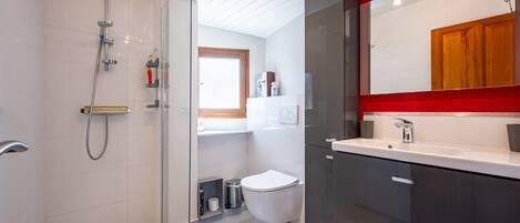 Et moderne badeværelse med en glas brusekabine, toilet og et spejl med tilhørende håndvask.