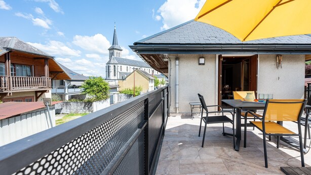 A balcony with a table and chairs, a yellow umbrella, and a church in the background. - Cottage 'Marie Andre' with Private Terrace and Wi-Fi (Entrelacs)