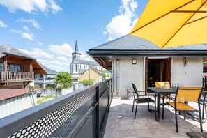 A balcony with a table and chairs, a yellow umbrella, and a church in the background. - Cottage 'Marie Andre' with Private Terrace and Wi-Fi (Entrelacs)