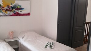 Ein Schlafzimmer mit zwei Betten, einem Nachttisch mit Lampe, einem Bild an der Wand und einer Tür zu einem anderen Raum.