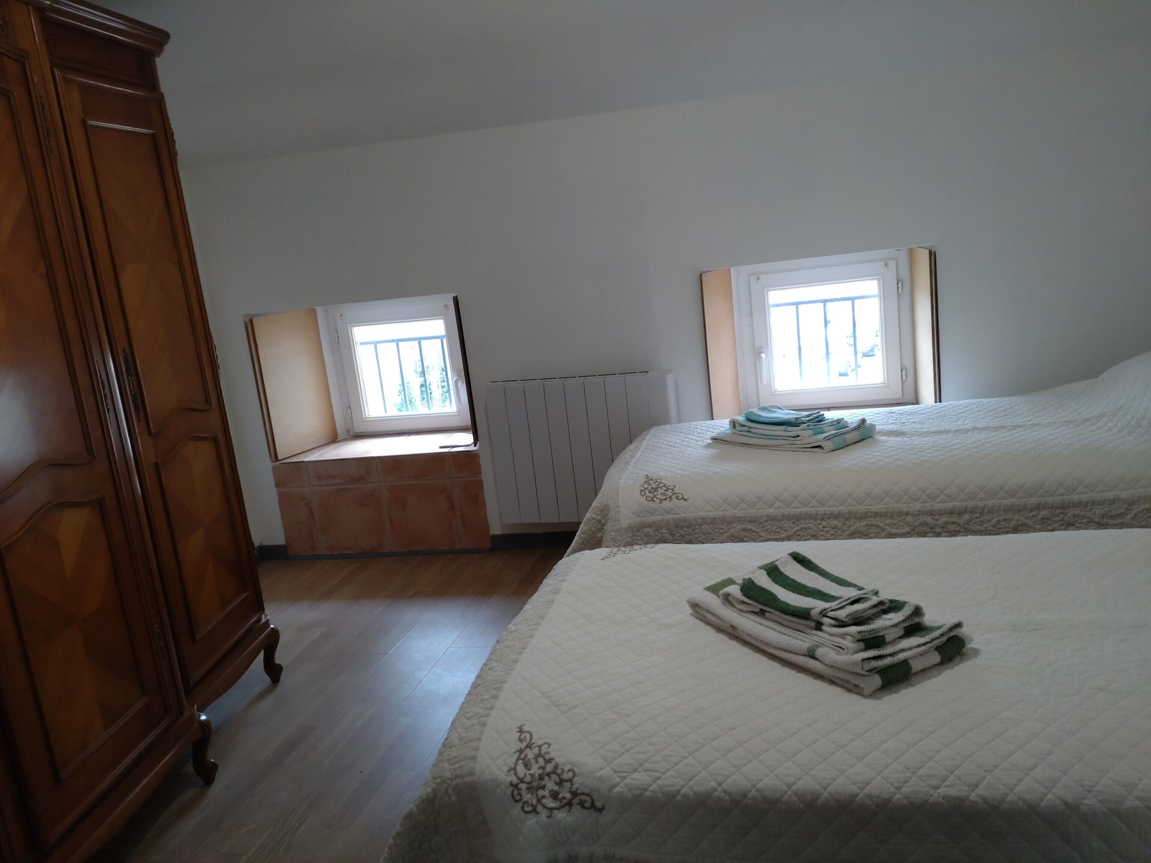 Ein Schlafzimmer mit zwei Betten, einem Holzschrank, einem Heizkörper und einem Fenster.