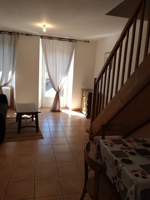 A living room with a wooden staircase, a dining table with a patterned tablecloth, and a chair.