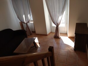 Een kamer met een eettafel, stoelen, een bank en gordijnen.