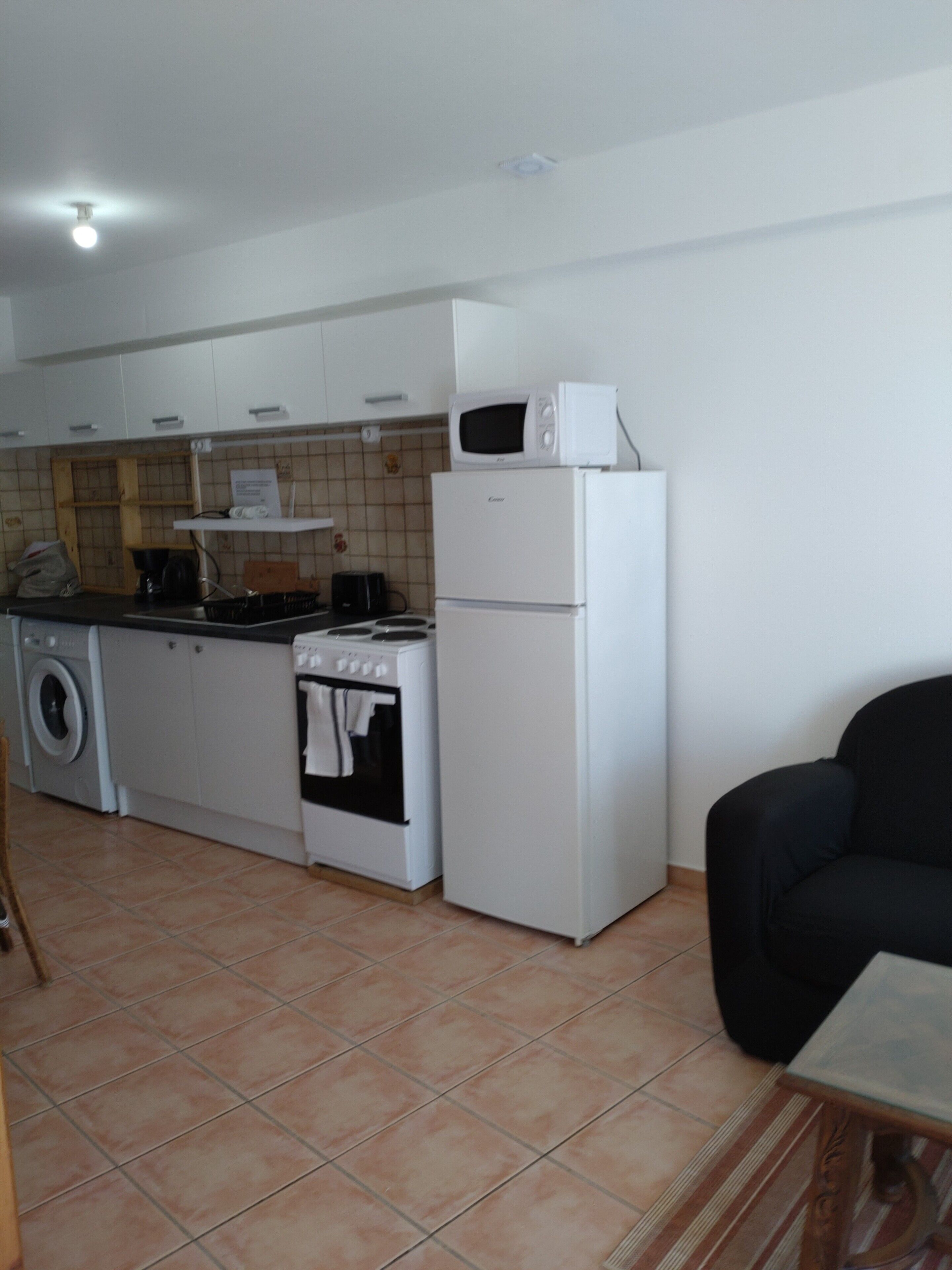 A compact kitchen with a washing machine, stove, microwave, and refrigerator.