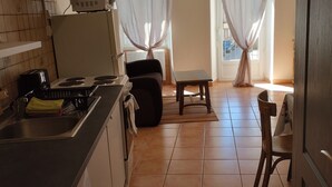 Eine Küche mit Waschmaschine, eine Essecke mit Tisch und Stühlen sowie ein Blick ins Freie durch Vorhänge.