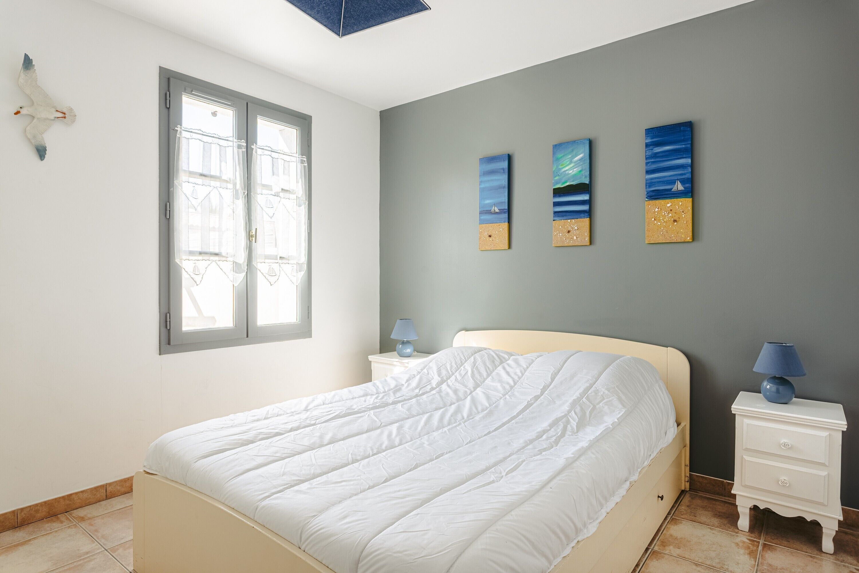 Un dormitorio con cama, mesita de noche, lámpara y ventana.