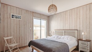 Ein Schlafzimmer mit einem Bett, einem Sessel, einem Nachttisch, einer Lampe, einem Bilderrahmen und einem Fenster.