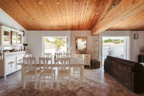 Un espace repas doté d’un plafond en bois, de meubles blancs et offrant une vue sur l’extérieur.