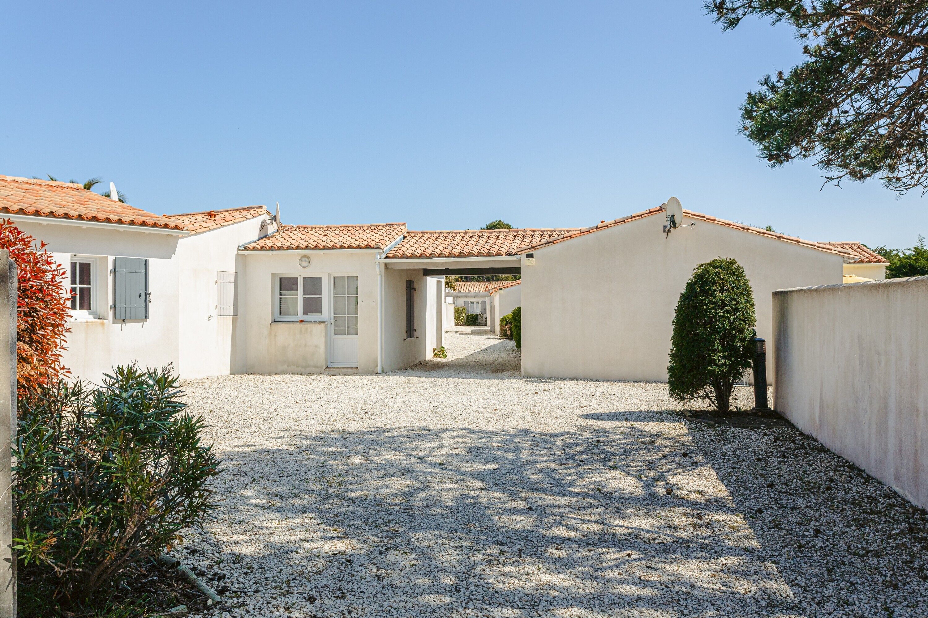 A residential property with a gravel driveway, white walls, and a tiled roof.