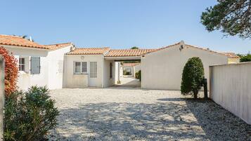 A residential property with a gravel driveway, white walls, and a tiled roof.