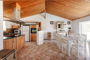 Une cuisine dotée de meubles en bois, d’un îlot central et d’un coin repas avec des chaises blanches.