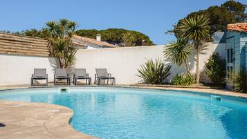 A swimming pool with lounge chairs, palm trees, and a white building with a tiled roof.